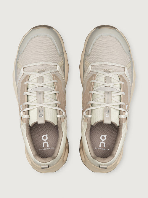 Pair of beige sneakers with white laces on a light gray background