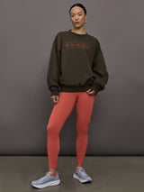 Model wears an oversized brown crewneck sweatshirt with the words 'Worldwide Modern' printed in coral coloring across the chest.