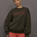 Model wears an oversized brown crewneck sweatshirt with the words 'Worldwide Modern' printed in coral coloring across the chest.