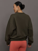 Model wears an oversized brown crewneck sweatshirt with the words 'Worldwide Modern' printed in coral coloring across the chest.