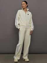 Model wears an off white track jacket with royal blue seam detailing down the sleeves. 