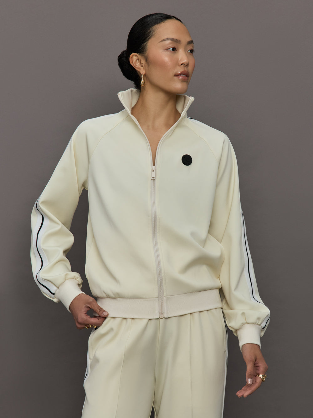 Model wears an off white track jacket with royal blue seam detailing down the sleeves. 