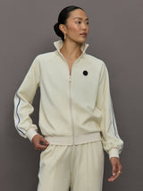 Model wears an off white track jacket with royal blue seam detailing down the sleeves. 