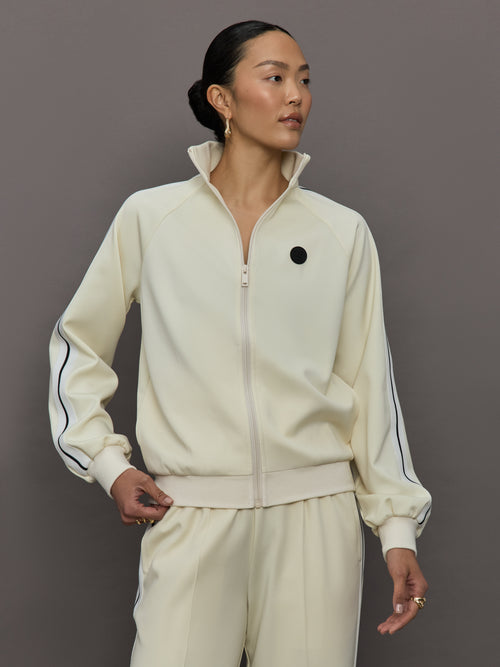 Model wears an off white track jacket with royal blue seam detailing down the sleeves. 
