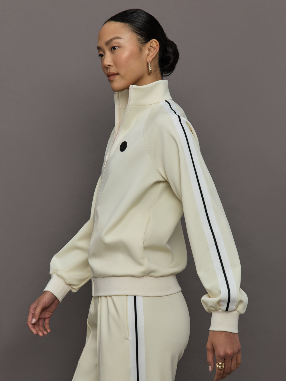 Model wears an off white track jacket with royal blue seam detailing down the sleeves. 