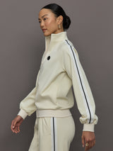 Model wears an off white track jacket with royal blue seam detailing down the sleeves. 