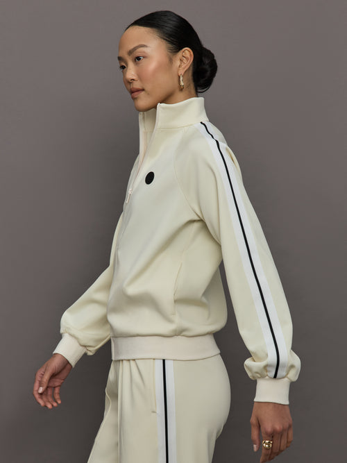 Model wears an off white track jacket with royal blue seam detailing down the sleeves. 