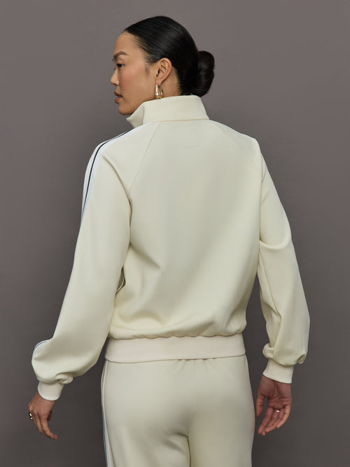 Model wears an off white track jacket with royal blue seam detailing down the sleeves. 
