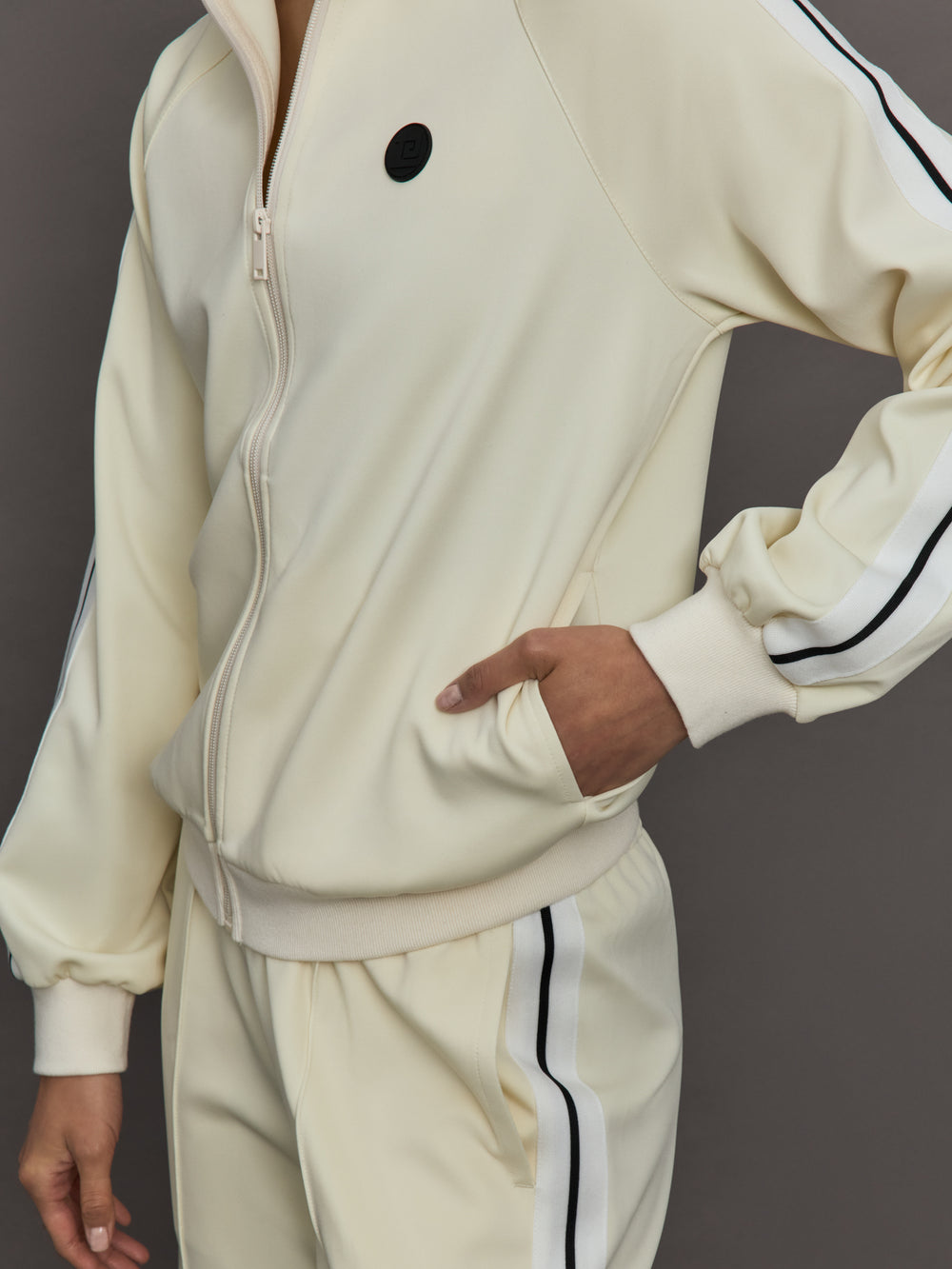 Model wears an off white track jacket with royal blue seam detailing down the sleeves. 