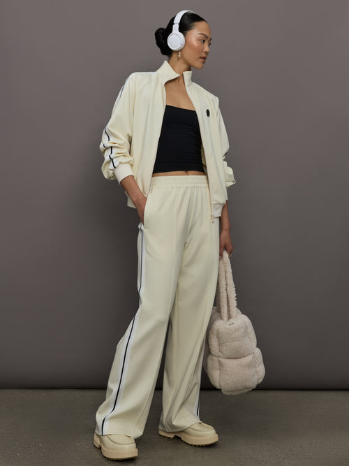 Model wears an off white track jacket with royal blue seam detailing down the sleeves. 