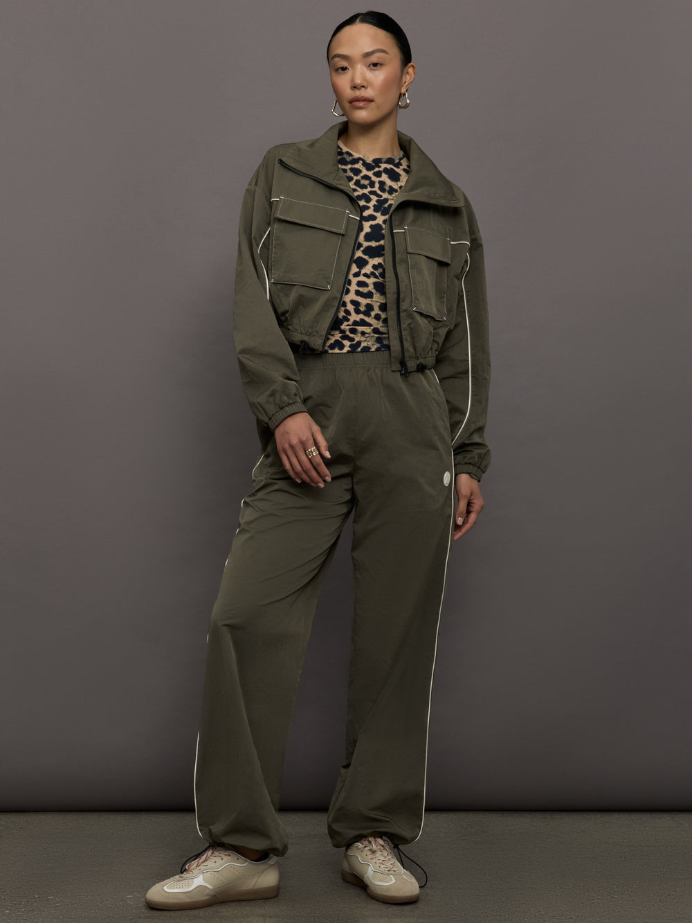 Model wears an olive colored cropped bomber with symmetrical chest pockets and white seamed detailing. 