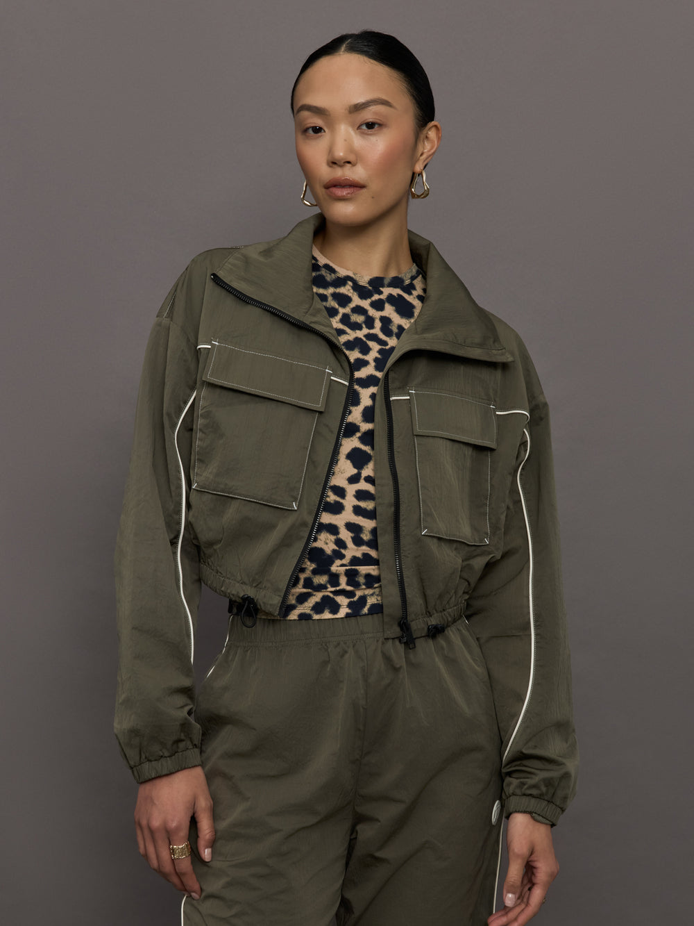 Model wears an olive colored cropped bomber with symmetrical chest pockets and white seamed detailing. 
