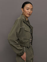 Model wears an olive colored cropped bomber with symmetrical chest pockets and white seamed detailing. 