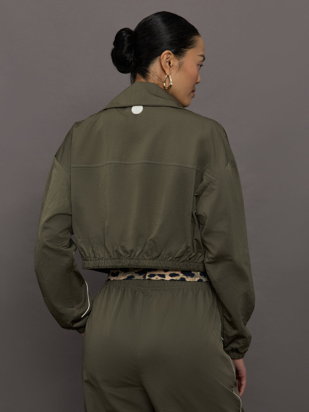 Model wears an olive colored cropped bomber with symmetrical chest pockets and white seamed detailing. 