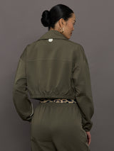 Model wears an olive colored cropped bomber with symmetrical chest pockets and white seamed detailing. 