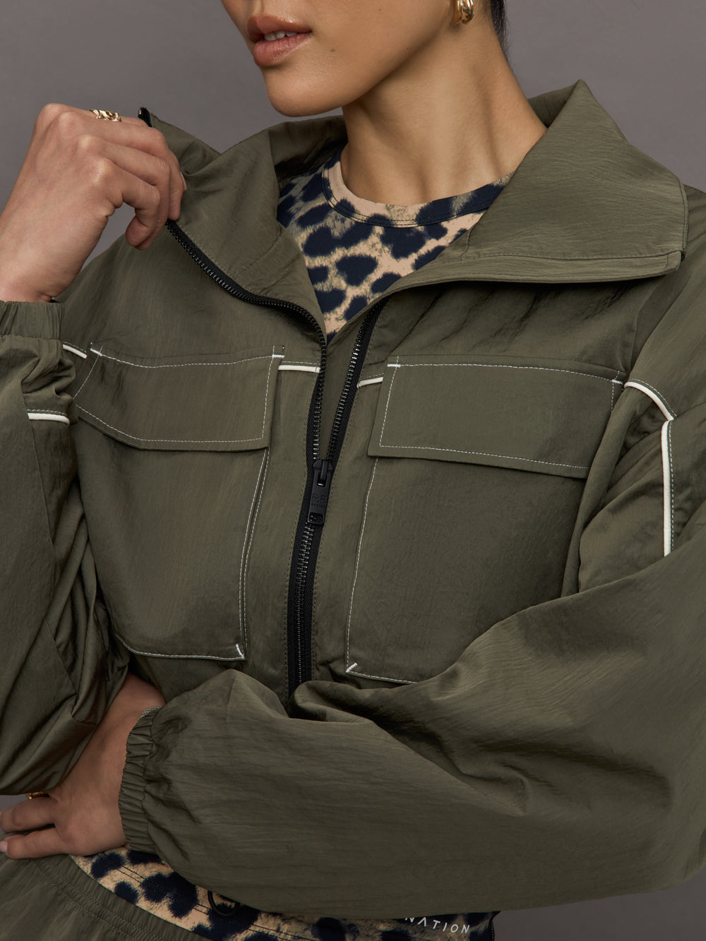 Model wears an olive colored cropped bomber with symmetrical chest pockets and white seamed detailing. 