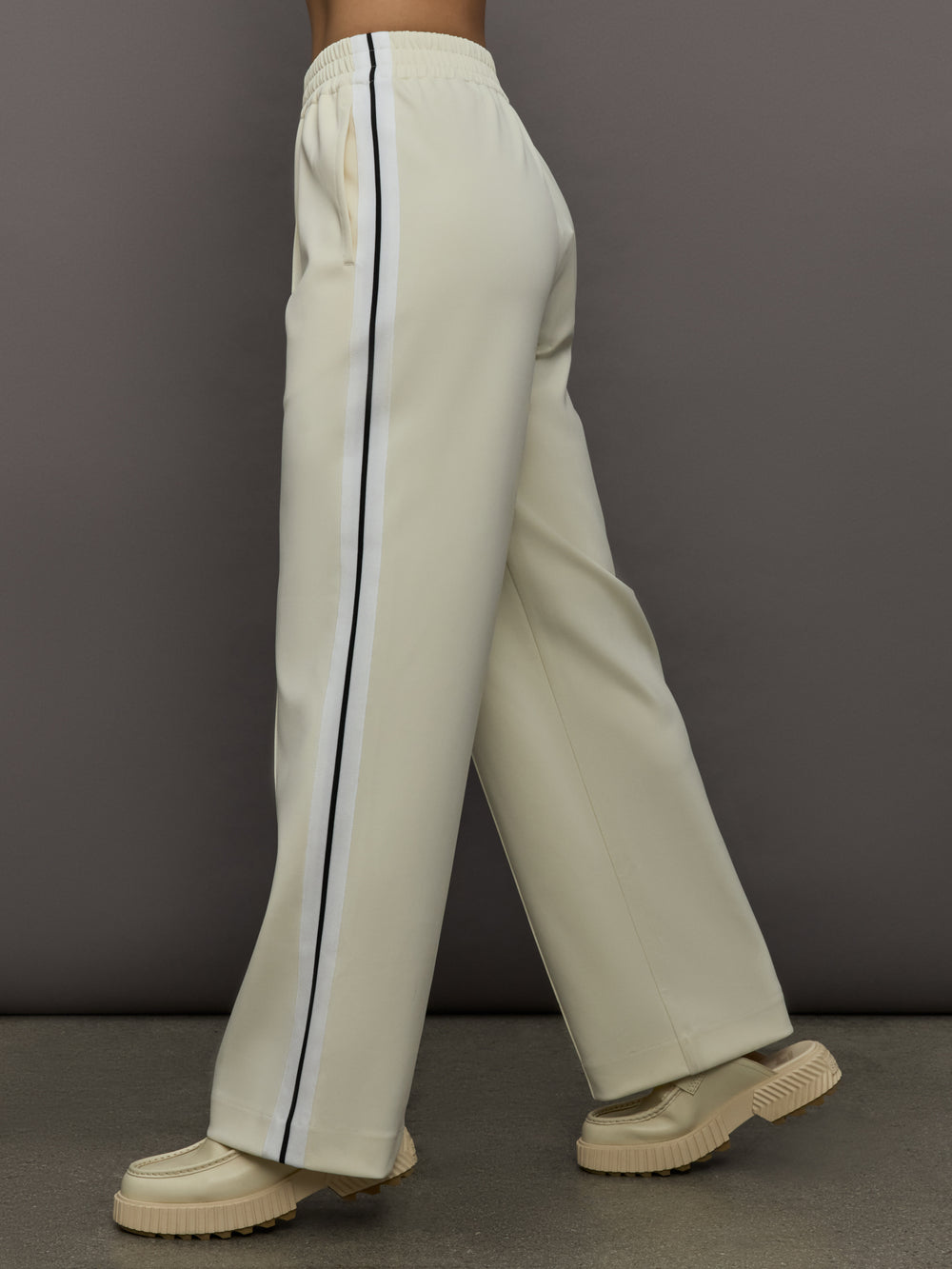 Model wears an off white track pant with blue seamed detailing down the sides. 