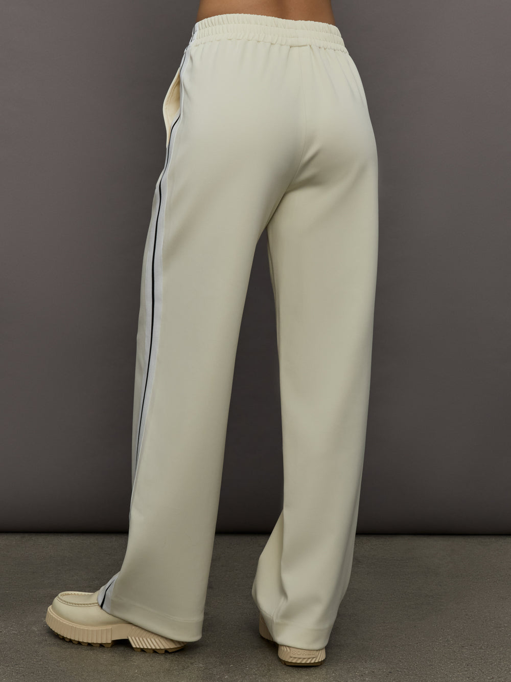 Model wears an off white track pant with blue seamed detailing down the sides. 