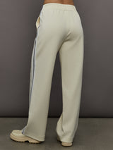 Model wears an off white track pant with blue seamed detailing down the sides. 