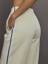Model wears an off white track pant with blue seamed detailing down the sides. 