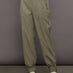 Model wears khaki track pant with large front pockets and cuffed ankles. 