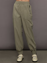 Model wears khaki track pant with large front pockets and cuffed ankles. 