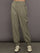 Model wears khaki track pant with large front pockets and cuffed ankles. 