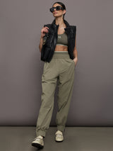 Model wears khaki track pant with large front pockets and cuffed ankles. 
