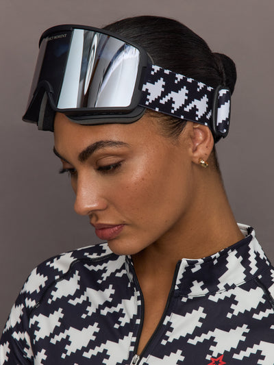 Side profile of ski goggles with reflective lens and adjustable black and white houndstooth strap.