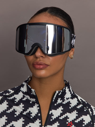 Front view of model wearing ski goggles with mirrored lens and black and white houndstooth strap.