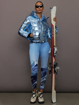 Full body view of Polar Flare Ski Jacket III Light Blue Foil styled with printed leggings and ski equipment.