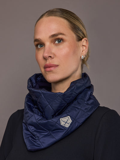 Woman wearing a navy quilted scarf against a gray background