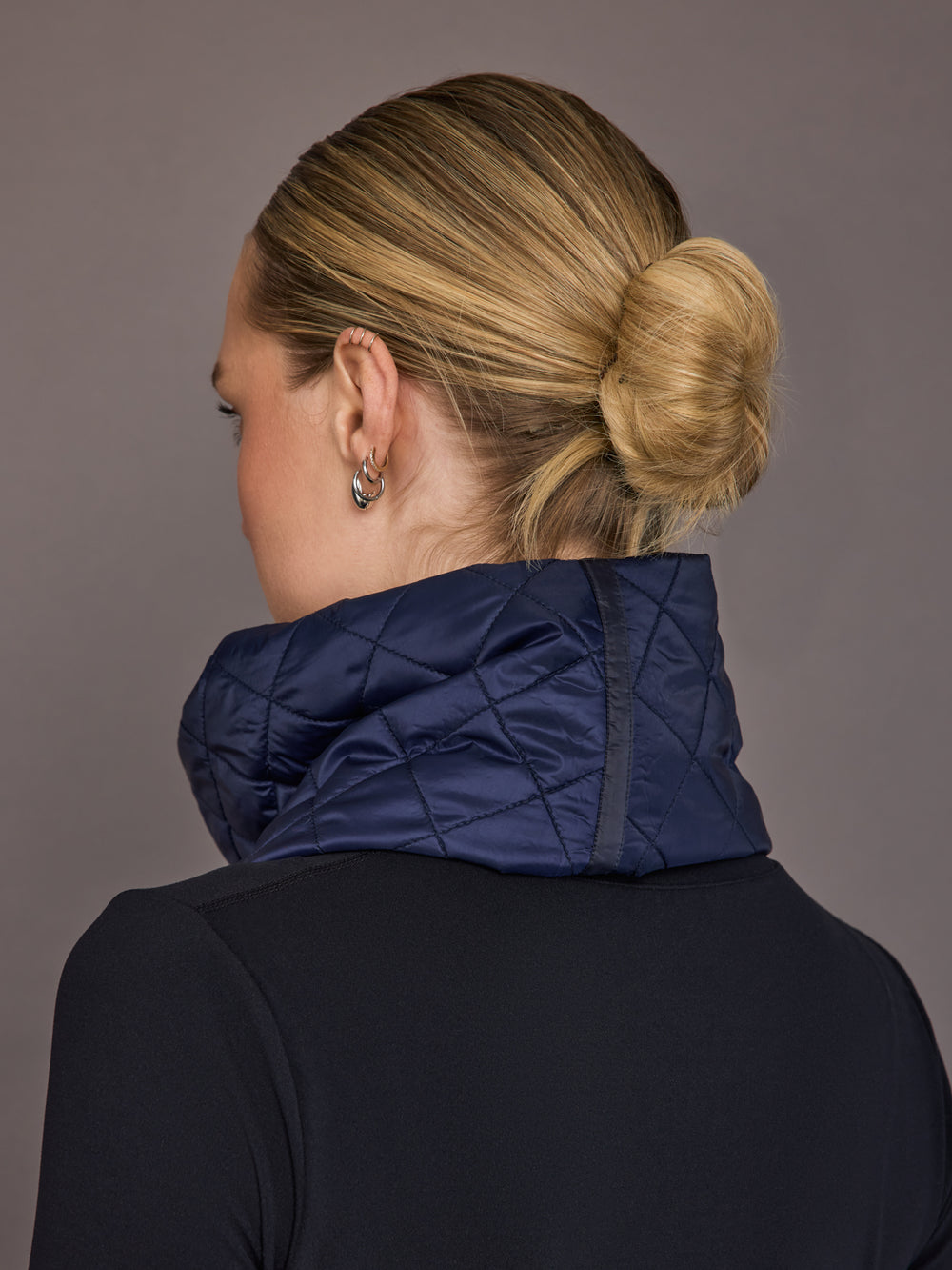 Person wearing a navy quilted jacket with a plain background