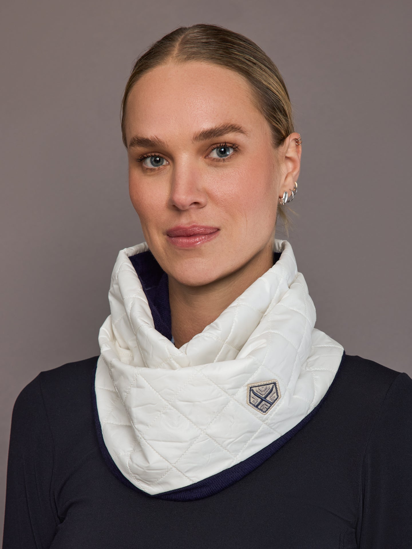 Woman wearing a white quilted scarf with a brand logo against a gray background