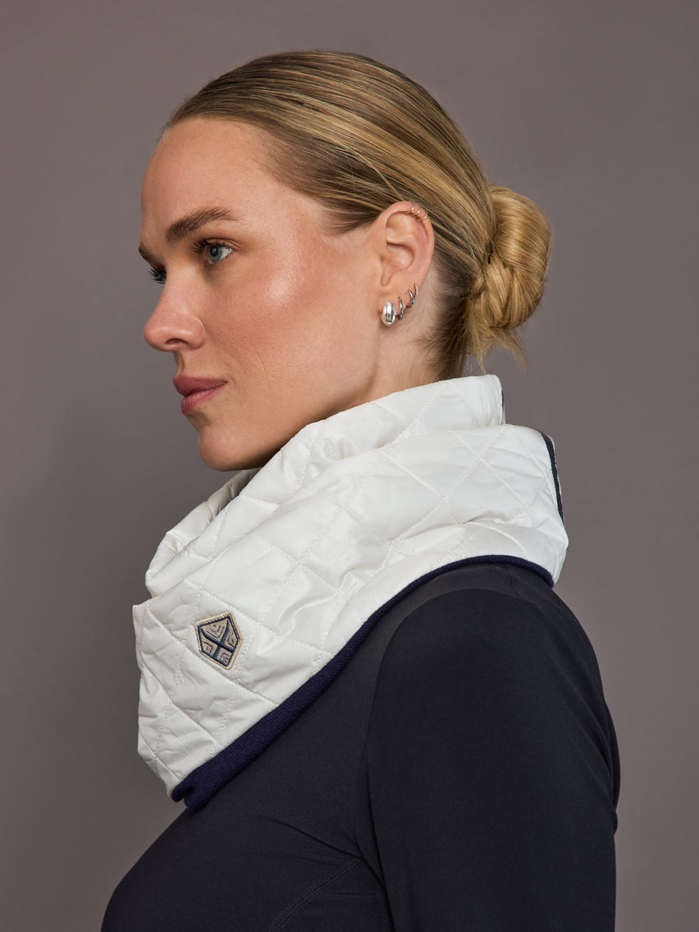 Woman wearing a white quilted scarf with a brand logo against a gray background