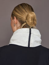 Person wearing a white quilted jacket with a dark collar against a gray background