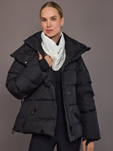 Person wearing a black puffer jacket with a white scarf against a gray background