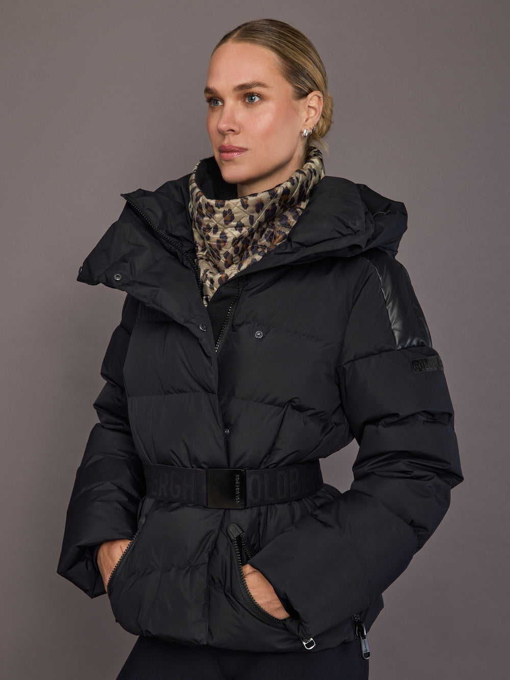 Woman wearing a black puffer jacket with a leopard print scarf against a gray background