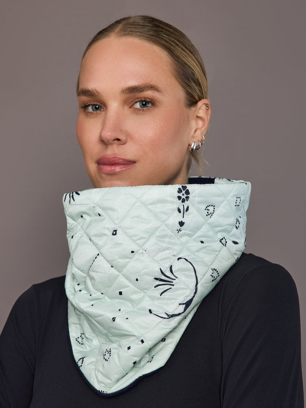 Person wearing a light green quilted scarf with black floral patterns on a plain background