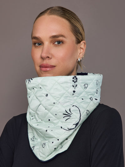 Person wearing a light green quilted scarf with black floral patterns on a plain background
