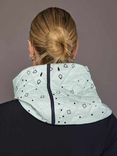 Person wearing a light green quilted scarf with black floral patterns on a plain background