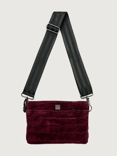 Burgundy suede handbag with a black seat belt strap 