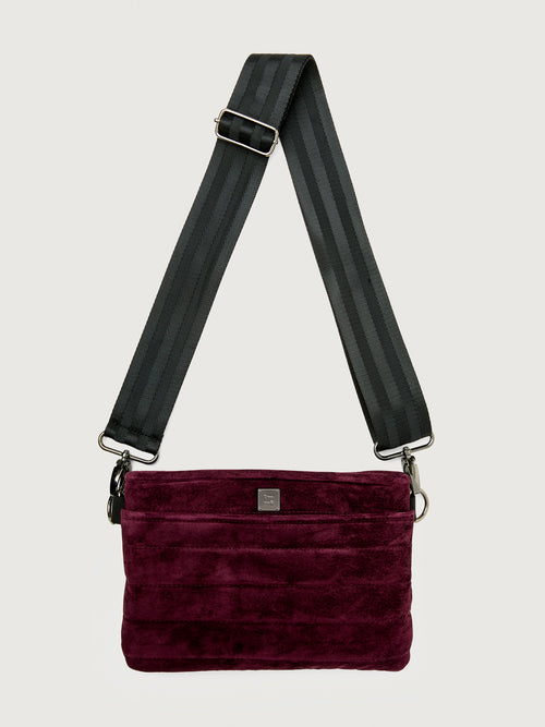 Burgundy suede handbag with a black seat belt strap 