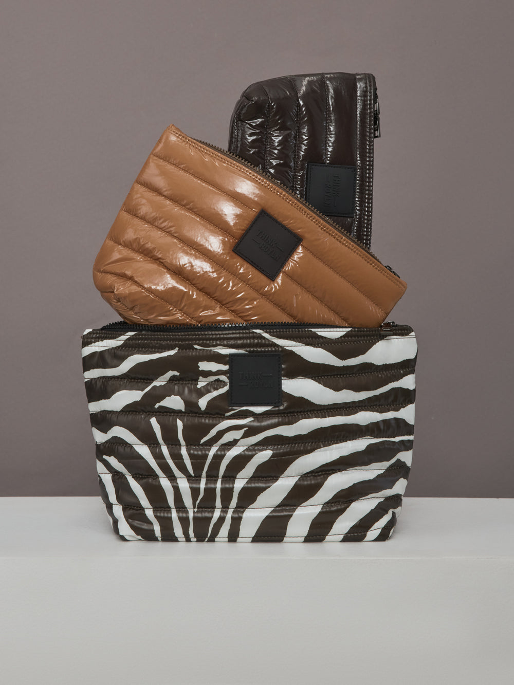 Stacked view of Travel Trio pouches in glossy nude and chocolate finishes.