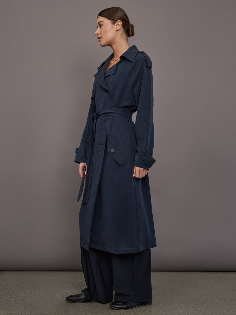 Model is wearing Elva Trench Coat in Navy, side profile view with relaxed silhouette.