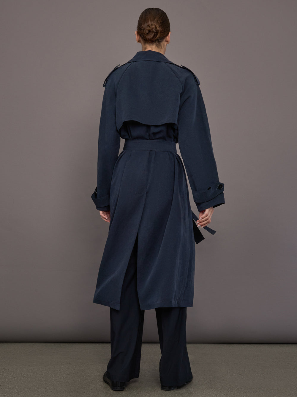 Model is wearing Elva Trench Coat in Navy, full back view with belt and vent detail.