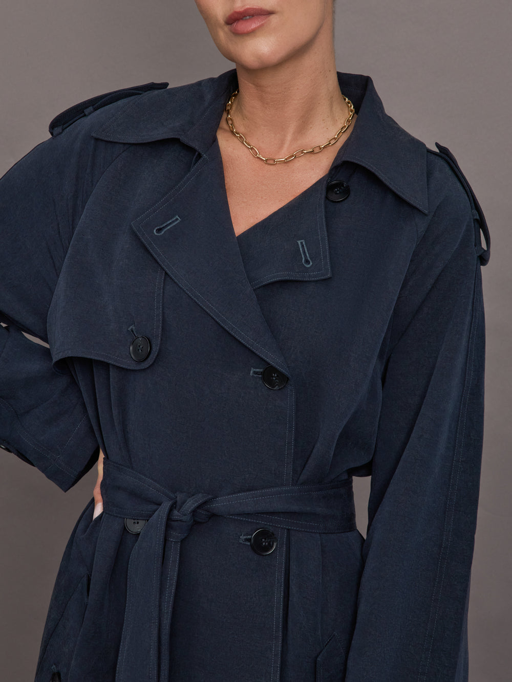 Model is wearing Elva Trench Coat in Navy, close up of lapel and button detailing.
