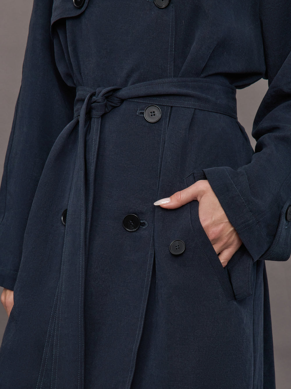 Model is wearing Elva Trench Coat in Navy, close up of waist belt and pocket detail.