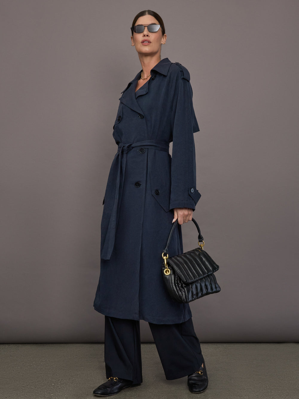 Model is wearing Elva Trench Coat in Navy, full body styling with handbag and sunglasses.