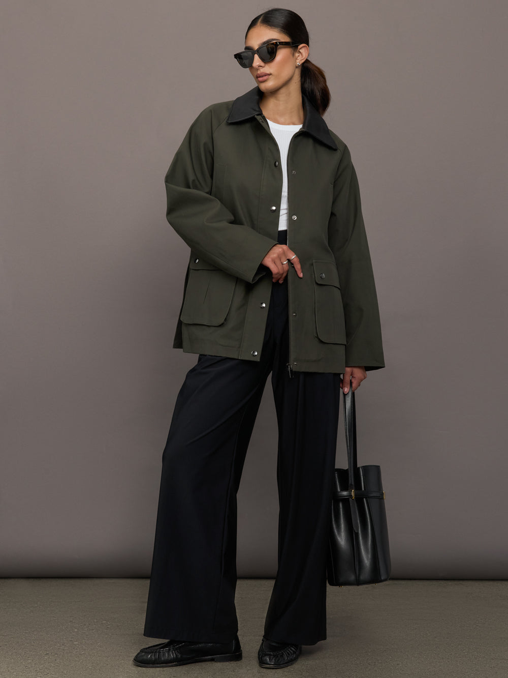 Model is wearing the utility barn jacket in dark olive, full body with sunglasses.